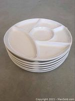 Stack of six white ceramic fondue plates with multiple compartments visible from the side angle.