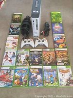Wide view of Xbox 360 console with two controllers, power cords, AV cable, and 16 games laid out on floor.