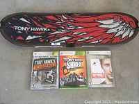 Top side view of Tony Hawk branded Xbox 360 skateboard controller with red, black, and white wing and maple leaf design, with 3 Tony Hawk games (Underground, Shred, Project 8) in front.
