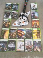 Photo showing 14 Xbox 360 game cases laid out with a white Guitar Hero 2 guitar controller in center