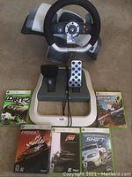 Photo showing Xbox 360 racing steering wheel with pedals and the five included Xbox 360 racing games arranged around the pedals.