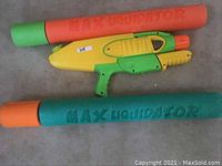 Three squirt guns including a yellow and green plastic squirt gun and two large foam squirt guns labeled Max Liquidator in orange and green.