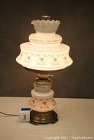 Front view of the entire assembled lamp showing milky white glass with floral decoration and ruffled top chimney glass.