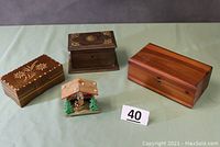 Four wooden boxes on green cloth: Lane cedar chest, carved music box, decorative wooden box, thermometer in cuckoo clock style case