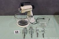 Sunbeam Mixmaster stand mixer with large and small glass bowls and four attachments (2 beaters, 2 bread hooks) laid out in front.