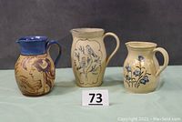 Lot of three art pottery pitchers positioned side by side showing overall appearance and relative sizes.