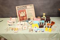 Wide shot showing assembled dollhouse, boxed Petite Princess furniture items spread around, including pink chaise lounges, blue lounge, dining sets, piano, kitchen and bathroom furniture.