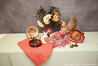 Full lot arranged on a table including rooster figurine, plates, raffia balls, vase with flowers, tablecloth, basket, and other smaller items.