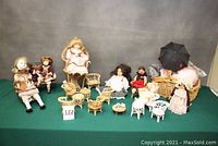 Full lot of 8 dolls, 15 pieces of wicker doll furniture, and accessories displayed on table