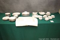 Full lot overview showing organized dinnerware, cups, bowls, and linens on green tablecloth