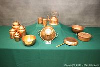 Full view of all copper items on green cloth including canisters, shakers, teapot, colander, bowls, pot, and frying pan