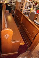 Side view of the eight-foot church pew showing the carved cross on one end and smooth wood finish along the length.