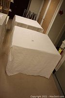 Two folding tables covered with custom white covers draping to floor in a hallway.