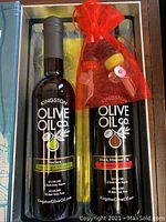 Photo of two bottles, one olive oil and one balsamic vinegar, with the red bag containing pouring nozzles placed beside the bottles inside the box.