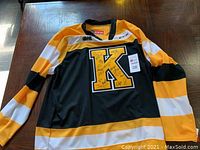 Front of the Kingston Frontenac hockey jersey showing orange, white, and black colors with a large letter K and autographs.