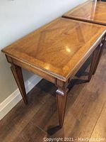 Side view of one wooden vintage side table showing geometrical inlay on tabletop and tapered legs with decorative detail.