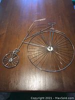 Photo of metal wireframe Penny-Farthing bicycle wall art laid flat on wooden surface showing full design and detail.