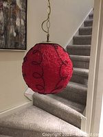 Full view of the red spherical lucite swag lamp with black wire swirl designs hanging near staircase.