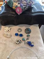 Vintage jewelry pieces arranged on a surface including earrings, rings, and a black vintage jewelry box with a bag of additional items on top.