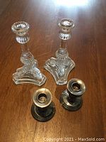 Two pairs of candlestick holders shown together on a wooden surface. One pair is vintage English silver plate with a patina, the other clear glass.