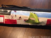 Photo of the black carrying case with a label showing the green Ventura Mini Shelter tent pitched on a sandy beach along with kids playing in the background.