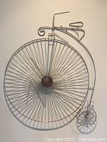 Front view of the metal Penny-Farthing bicycle wall art showing the entire piece flat against the wall.