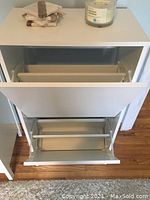 Front view of white shoe cabinet with two compartments open, showing metal bars inside for shoe holding.
