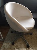 Front-side angle showing the white curved seat and metallic swivel base with wheels on a light rug.