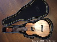 Ukulele and matching black hard case open, showing the front of the ukulele with natural wood grain finish and fretboard.