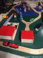 View of wooden trains, tracks, buildings, and painted tabletop with river and green land areas.