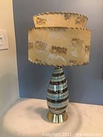 Full view of the lamp showing the base and double-tiered lampshade with patterned fabric and scalloped edges.