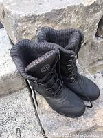 Front angle photo of the two black boots showing the laces and padded ankle collar, placed on stone.