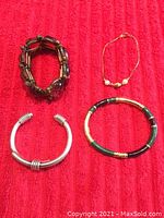 Four bracelets arranged on red fabric: Mexican sterling silver cuff, green-black enamel bracelet, gold bracelet with pearls, brown bead costume bracelet.