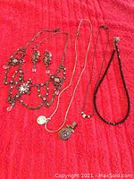 Four jewelry pieces displayed on red background: ornate necklace with earrings, sterling silver chain necklace, purple stone pendant, and black beaded necklace.