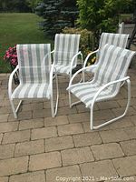 Full view of four aluminum sling chairs with green and white striped fabric seated on a stone patio in outdoor setting