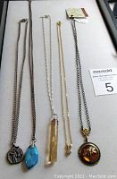 Five pendant necklaces displayed flat on a white surface, showing the entire length and pendants clearly.