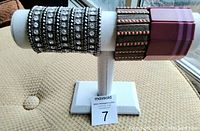 Display with four fashion bracelets: two wide black textured stretch bracelets with silver bead accents, and two chunky rectangular purple/pink resin bangle bracelets.