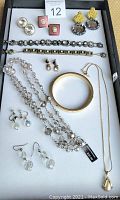 Photo showing an assortment of designer jewelry including necklaces, bracelets, bangle, and various styles of earrings placed on a white tray.