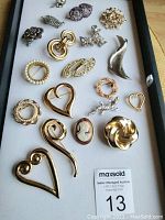 Brooch lot laid out flat on white background showing all pieces together, including various shapes and sizes like hearts, flowers, geometric and animal motifs.