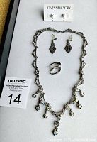 Top view of jewelry laid out on display tray, showing silver-tone necklace with crystal-like accents, two pairs of earrings (filigree drop and pearl studs), and a silver-tone ring.