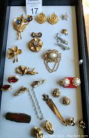 Full tray view showing assortment of gold-tone vintage jewelry including brooches, earrings, and necklaces arranged flat on white surface.
