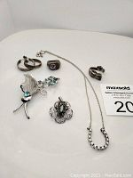 Photo showing various sterling silver jewelry pieces arranged on a white surface including rings, a necklace, pendants, and a brooch.