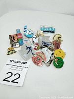 Photo of assorted enamel pins including event, sport, and brand-themed pins arranged on white background with auction tag.