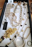 Overview of fashion jewelry pieces arranged on a black tray including chunky gold and silver chains, bangles, and pendant necklace