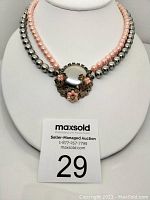 Front view of the vintage two-strand beaded necklace displayed on a white bust stand showing pink and silver beads meeting at a decorative clasp with floral and rhinestone details.