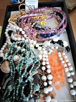 Multiple assorted beaded necklaces piled in a tray, showing pink, white, blue, peach, yellow, and turquoise beads.