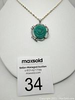 Front view of pendant with carved amazonite stone showing floral design on a white display stand, with chain lying above.