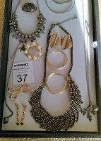 Top-down view of assorted costume jewelry laid out on a white tray including necklaces, earrings, bracelets, and brooches.