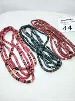 Photo showing three long strands of old beads laid out on white surface, colors varying rose red, dark green/teal, cream and black.