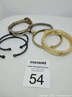 Photo showing five assorted bangles of various metal finishes including gold-tone filigree, silver twisted, black twisted open cuff, gold with clasp, and bronze rhinestone accented.